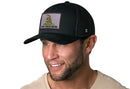 A man smiles while wearing a Haka Hat Dont Tread On Me Trucker Hat, a black snapback by Haka Hat featuring a Gadsden Flag tactical patch with a coiled snake and the words DONT TREAD ON ME.