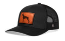 The Haka Hat Doberman Trucker Hat Leather by Haka Hat is a black mesh snapback trucker hat with a curved bill and a brown rectangular leather patch featuring a dog silhouette on the front panel.