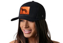 A woman smiles wearing the Haka Hat German Shepherd Trucker Hat, a black snapback by Haka Hat featuring an orange leather patch with a dog silhouette. The background is plain white.