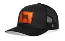 The Haka Hat Pug Trucker Hat Leather is a black mesh snapback by Haka Hat, featuring an orange leather patch with a dog silhouette on the front panel.