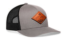 The Haka Hat Diamond Mountain and Trees Trucker Hat Leather is a gray-black snapback featuring a mesh back and a brown leather patch with a mountain and sun design on the front.