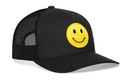 The Haka Hat Smiley Face Trucker Hat is a black mesh snapback with a curved brim and a large yellow embroidered smiley face patch on the front.