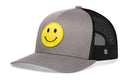 The Haka Hat Smiley Face Trucker Hat features a gray front, black mesh back, yellow emoji patch, and a comfort-fit snapback for all-day wear.