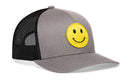 The Haka Hat Smiley Face Trucker Hat in gray-black features a comfort-fit snapback, black mesh back, and a yellow embroidered emoji patch on the front.