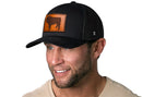 A smiling man with a trimmed beard wears the Haka Hat English Bulldog Trucker Hat Leather | Black Dog Snapback by Haka Hat, paired with a beige shirt, standing against a white background.