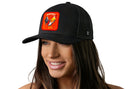 A woman with long brown hair smiles while wearing the Haka Hat Rooster Energy Trucker Hat, a black snapback featuring a colorful rooster and "energy" on an embroidered patch, by Haka Hat. The hat stands out against a white background.