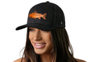 A woman with long brown hair smiles while wearing the Haka Hat Salmon Trucker Hat (Black Salmon Snapback) by Haka Hat, featuring an orange fish graphic and comfort-fit sweatband against a plain white background.