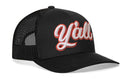 The Haka Hat Y'all Trucker Hat is a black mesh snapback that channels the western lifestyle, featuring "Y'all" boldly embroidered in white and red script on the front.