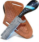The Texan Knives Custom Handmade Bull Knife – Fall Damascus Steel Edition features a patterned blade, black handle with blue inlay, and comes with a brown stitched leather sheath—ideal for fall hunting.