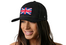 A smiling woman wears the Haka Hat United Kingdom Flag Trucker Hat, a black UK Union Jack snapback by Haka Hat, featuring a United Kingdom flag patch on the front against a white background.