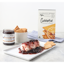 A log of cheese topped with dark berry jam is served on a rectangular white plate with Terrapin Ridge Farms Cinnamon Crackers. Nearby are a jar of Terrapin Ridge Farms jam, a dish of cheese pairings, and the crackers’ box.