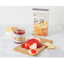 A cutting board features cream cheese with Terrapin Ridge Farms Red Pepper Jelly, surrounded by crackers. In the background are a jar of Terrapin Ridge Farms Red Pepper Jelly and sea salt gourmet crackers—ideal for an appetizer spread.