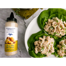 A bottle of Terrapin Ridge Farms Ginger Yuzu Aioli Squeeze, a tangy umami sauce, sits beside a white plate with three tuna salad lettuce wraps on a marble surface.