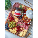 A wooden cheese board with assorted cheeses, salami, crackers, olives, grapes, blueberries, almonds, figs, and a jar of Terrapin Ridge Farms Hot Pepper Bacon Jam—perfect for charcuterie boards.