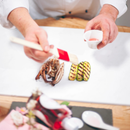 A chef uses a brush to glaze sliced grilled zucchini and mushrooms on a white plate, holding a small cup of Taycte Acetaia Malpighi Prelibato Rosé Balsamic Vinegar — Pink Italian Condimento, Delicate & Fruity in the other hand.
