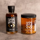 Spice Witch Chili Oil + Chili Crisp, both from Spice Witch, are shown together on a neutral surface with a light textured backdrop.