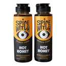 Two bottles of Spice Witch Hot Honey Duo—a sweet, spicy chili honey—come with orange and black labels featuring a stylized eye. The labels read "100% Magical – 0% Boring" and showcase this woman-owned, Asheville, NC brand.