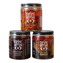 Spice Witch Chili Crisp Box of 3 jars—Chili Crisp, Black Garlic, and Spicy Honey—features bold white text and an eye logo on handcrafted labels, displayed stacked on a gray surface.