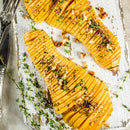 Butternut squash halves roasted and seasoned with SALTOPIA Infused Sea Salts' Ultimate Veggie Lover Salts, topped with fresh thyme and chopped nuts, served on a rustic board with cutlery.