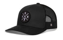 The Haka Hat Vermont Trucker Hat | Black VER X Snapback features a solid fabric front and bill, black mesh sides and back, a snapback closure, and a round patch with crossed lines, E/V/R letters, and a small pistol icon.