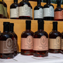 Bottles of Under The Bark Syrup Co Coffee Maple Syrup are displayed on wooden shelves, each featuring a colorful maple leaf logo and flavors like Maple, Cinnamon, and Chai.