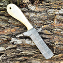 The Texan Knives Gareth Bull Style Knife features an 8" Damascus steel blade and a smooth camel bone handle, shown resting on rugged tree bark. Includes a Western leather sheath.