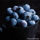 A close-up of fresh blueberries covered in water droplets, piled high in a black cup against a dark background. The image evokes the rich flavors of Modena, Italy, reminiscent of Georgetown Olive Oil Co.’s Wild Blueberry Balsamic Vinegar. Text at the bottom right reads Designed by Freepik.