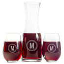 A Wine Decanter - The Medalist and two stemless wine glasses filled with red wine, each engraved with a circular emblem featuring the letter M.