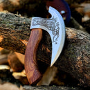 The Texan Knives Custom Hand-Engraved Axe Pizza Cutter features an 8" J2 steel blade with intricate Celtic knot designs and a wooden handle, resting against a stack of cut logs.