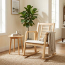 The DirectDeals Wooden Rocking Chair with Upholstered Seat and Ladder Back, draped with a blanket, sits by a small round table with a mug and book in a cozy, sunlit room with a potted plant and woven rug.