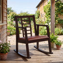 The DirectDeals Wooden Rocking Chair with Upholstered Seat and Ladder Back sits on a stone patio, surrounded by potted plants near a house with flowers and greenery under a sunny sky.