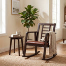 The DirectDeals Wooden Rocking Chair with Upholstered Seat and Ladder Back sits by a round side table with a mug and book, surrounded by sunlight, a potted plant, and cozy neutral decor.