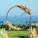 A large circular wedding arch with flowers and pampas grass stands on green grass beside a 43.5 Inch Folding Kids Picnic Table & Bench Set No Assembly Wooden Toddler Table by DirectDeals, with the ocean and a wooden fence in the background.