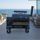 A pair of BBQ Boards® Yoder YS1500 Front & Pellet Bin Cutting Boards sits on a large black smoker grill beside a BBQ prep station, set on a patio with cushioned seating overlooking the calm blue ocean and clear sky.