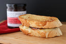 A grilled cheese sandwich with melted cheese sits beside a jar of Terrapin Ridge Farms Hot Pepper Bacon Jam—perfect for charcuterie boards or adding bold, gourmet flavor to snacks.