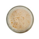 Top-down view of a glass jar filled with SALTOPIA Infused Sea Salts' Saltopia Lemon Cheesecake Sugar: ZEST FOR LIFE—light beige with golden-brown flecks—set against a white background.