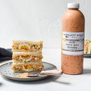 Egg salad sandwiches rest on a plate beside a bottle of Terrapin Ridge Farms Zesty Seven Spice Dressing. Some of the zesty dressing is spread on the sandwich and plate, with a knife nearby.