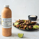 A bottle of Terrapin Ridge Farms Zesty Seven Spice Dressing sits beside grilled meat skewers with herbs and lime, and a bowl of rice in the background, offering an Asian-inspired experience from Terrapin Ridge Farms.