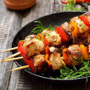 Grilled chicken skewers with red and yellow bell peppers are served on a black plate, garnished with fresh dill and infused with The Spice Lab Mediterranean Citrus Seasoning by The Spice Lab, set atop a rustic wooden table.