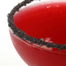 Close-up of a red cocktail in a glass rimmed with The Spice Lab Black Obsidian Salt Cocktail Rimmer by The Spice Lab, set against a white background.