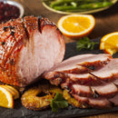 Sliced glazed ham with pineapples, orange slices, and parsley on a slate platter. Enhanced with a touch of The Spice Lab Organic Ground Vietnamese Saigon Cinnamon for added warmth and depth, this dish is truly memorable. Green beans and cranberry sauce are visible in the background.