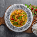 Enjoy a bowl of creamy yellow curry prepared with The Spice Lab Organic Indian Curry Powder, filled with vegetables and herbs, and served in a patterned dish on a wooden board alongside fluffy white rice, garnished with fresh cilantro and mint.