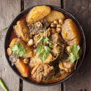A bowl of curry with tender meat, potatoes, carrots, bay leaves, chickpeas, and a garnish of fresh cilantro and The Spice Lab Fancy Chervil—an homage to French cooking by The Spice Lab—served on a rustic wooden table.