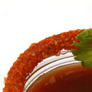A close-up of a glass rim coated with The Spice Lab Bloody Mary Salt Cocktail Rimmer by The Spice Lab, featuring a leafy green garnish and filled with a brown savory cocktail, set against a white background—perfect for elevating your favorite drinks.
