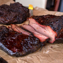 Slices of brisket with a dark, smoky crust and juicy pink interior sit on brown parchment paper, showcasing tender cooked meat infused with bold flavors from The Spice Lab Best Seller Seasoning Set by The Spice Lab.