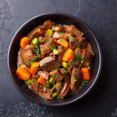 A bowl of beef stew with chunks of beef, carrots, celery, and herbs—such as The Spice Lab Ground Oregano from The Spice Lab for a fragrant Mediterranean herb twist—in a rich brown sauce, served on a dark textured surface.