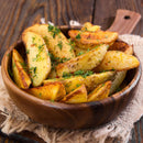 A wooden bowl filled with crispy potato wedges, garnished with chopped fresh herbs and a sprinkle of The Spice Lab Dill Weed Whole by The Spice Lab, sits on a rustic cloth and wooden table.