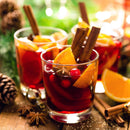 Three glasses of mulled wine, infused with The Spice Lab Mulling Spice and garnished with orange slices, cranberries, star anise, and cinnamon sticks, are surrounded by pinecones and festive greenery on a wooden table.