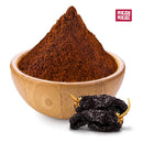 A wooden bowl filled with Rico Rico Ancho Chile Powder sits next to two dried chilies, evoking the rich flavors of Mexican cuisine. The Rico Rico logo appears in the top right corner.
