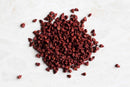 A pile of World Spice Annatto Seed by World Spice, known for its small, reddish-brown seeds often used as a natural food coloring and essential ingredient in achiote paste, is scattered on a white surface.